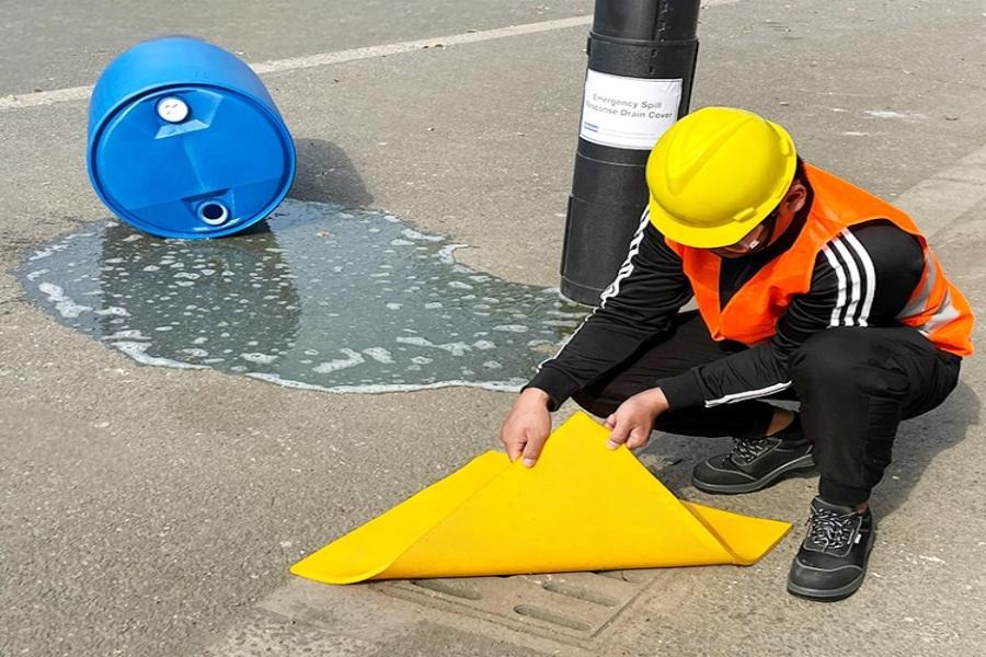 Worker deploying reusable polyurethane drain spill cover to prevent industrial runoff from entering storm drain